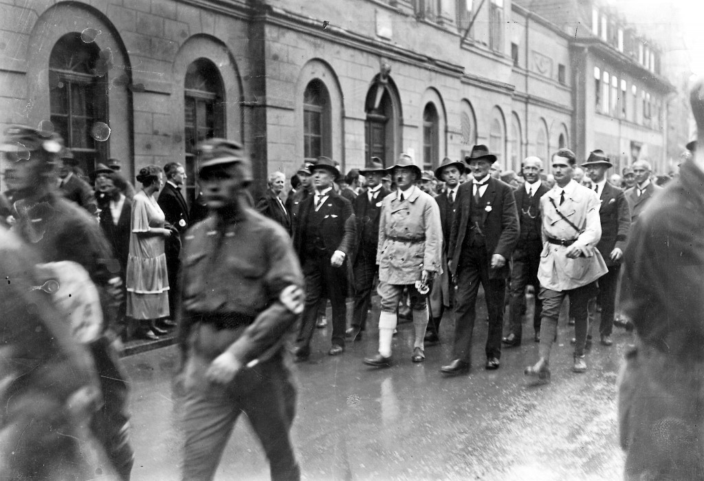 Adolf Hitler auf dem Propagandamarsch durch die Straßen Weimars während des ersten Reichsparteitages der NSDAP nach ihrer Neugründung. In der ersten Reihe Adolf Hitler (mit Hut) und ganz rechts Rudolf Heß. Zweite Reihe v. l.: Franz Xaver Schwarz, Alfred Rosenberg, Gottfried Feder und Heinrich Himmler. In der zweiten Reihe hinter Himmler geht Wilhelm Frick, 4. Juli 1926