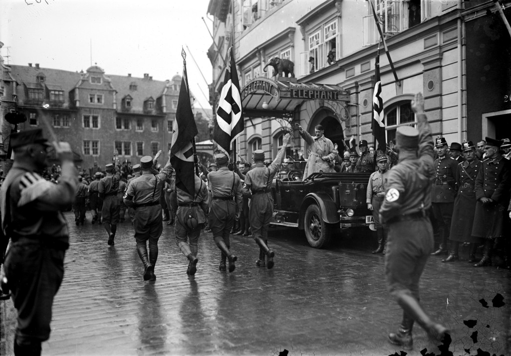 Marsch von SA-Männern vor dem Hotel Elephant, im Auto stehend Adolf Hitler, hinter ihm Rudolf Heß, halblinks hinter dem Auto Fritz Sauckel