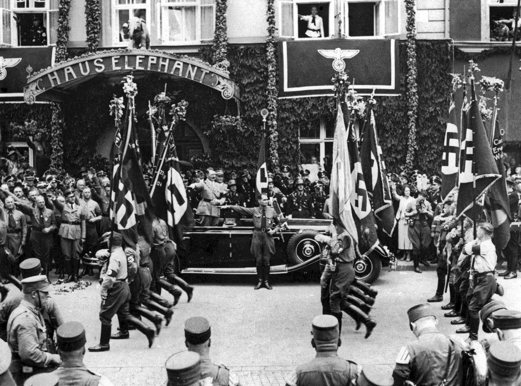 Adolf Hitler und Rudolf Hess (vor dem Auto) grüßen vorbeimarschierende SA-Truppen bei einem »Traditionsmarsch durch Weimar« mit dem Hitlergruß. Hinter dem Auto steht die »Blutfahne der Bewegung«, 5. Juli 1936