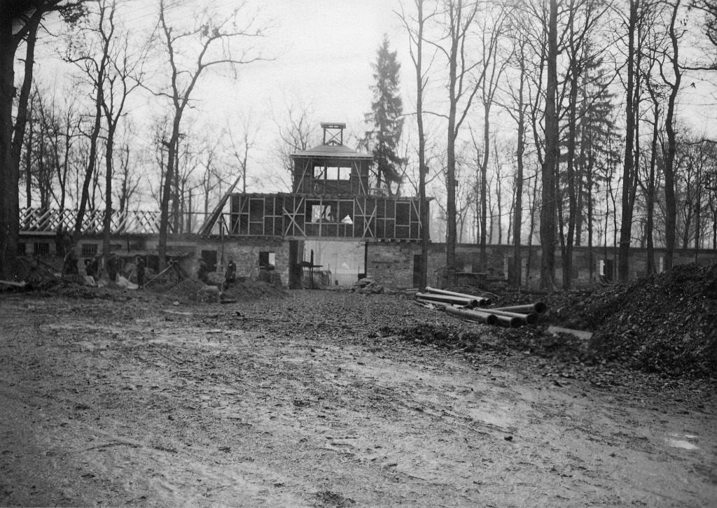 Blick vom »Carachoweg« auf das im Rohbau fertiggestellte Torgebäude zum Häftlingslager. Links ein Häftlingskommando bei Schachtarbeiten vor dem späteren Arrestzellenbau. 10. November 1937