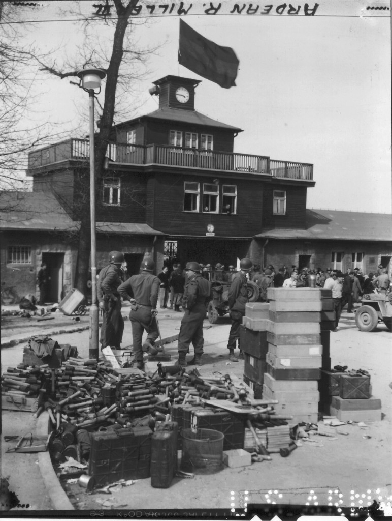 US-Soldaten vor dem Lagertor des befreiten KZ Buchenwald, im Vordergrund Munitionskisten und Handgranaten der SS, auf dem Torgebäude die schwarze Fahne anlässlich des Todes von Franklin D. Roosevelt, Präsident der USA, 18. April 1945